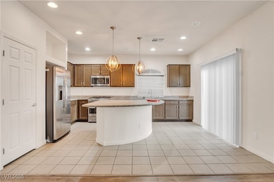 Kitchen with appliances with stainless steel finishes, light tile patterned floors, light stone counters, a center island, and pendant lighting