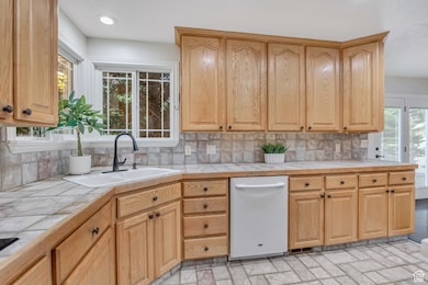 Kitchen featuring tile countertops, dishwasher, backsplash, and light brown cabinetry