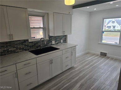 Kitchen featuring white cabinetry, tasteful backsplash, light stone countertops, light wood-type flooring, and recessed lighting