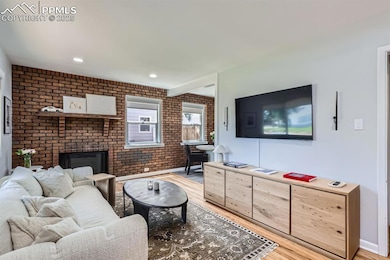 Living room with brick wall, light wood-style floors, a fireplace, and recessed lighting