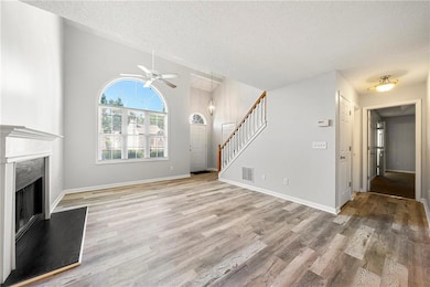 Unfurnished living room with stairway, light wood-style flooring, a fireplace with raised hearth, a textured ceiling, and ceiling fan