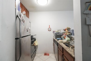 Kitchen with light tile patterned floors, a sink, brown cabinetry, stainless steel appliances, and light stone counters