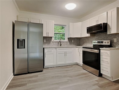 Kitchen featuring appliances with stainless steel finishes, ornamental molding, white cabinetry, and tasteful backsplash