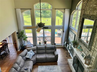 Living room featuring ceiling fan, healthy amount of natural light, a towering ceiling, a fireplace, and wood finished floors