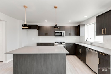 Kitchen featuring appliances with stainless steel finishes, pendant lighting, a kitchen island, light wood-style floors, and backsplash