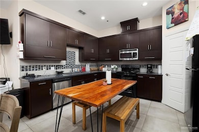 Kitchen with dark brown cabinetry, sink, tasteful backsplash, light tile patterned flooring, and appliances with stainless steel finishes