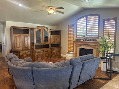 Living area with a fireplace, dark wood-style flooring, vaulted ceiling, and a ceiling fan