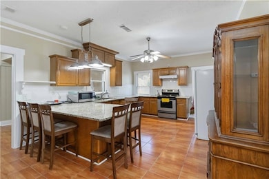 Kitchen with crown molding, decorative backsplash, brown cabinets, decorative light fixtures, and stainless steel appliances