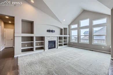 Unfurnished living room featuring built in shelves, vaulted ceiling, and a stone fireplace