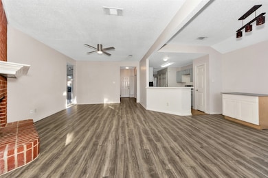 Unfurnished living room with dark wood-type flooring, a textured ceiling, a brick fireplace, and a ceiling fan