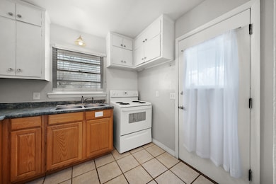 Kitchen featuring electric stove, dark countertops, light tile patterned floors, and brown cabinetry