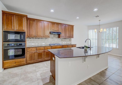 Kitchen featuring brown cabinets, tasteful backsplash, dark stone countertops, black appliances, and recessed lighting