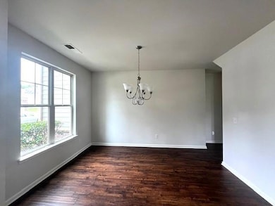 Spare room with dark wood-type flooring, a chandelier, and baseboards