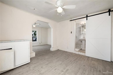 Empty room featuring a barn door, a ceiling fan, light wood-style flooring, and arched walkways