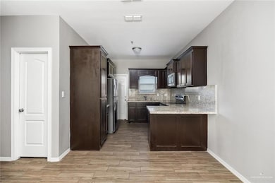 Kitchen featuring appliances with stainless steel finishes, dark brown cabinetry, a peninsula, light wood finished floors, and tasteful backsplash