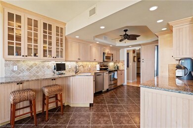 Kitchen with appliances with stainless steel finishes, granite counters, a raised ceiling, ceiling fan, and decorative stone backsplash and breakfast bar and stools