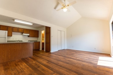 Kitchen featuring brown cabinetry, dark wood-style floors, freestanding refrigerator, lofted ceiling, and a textured ceiling