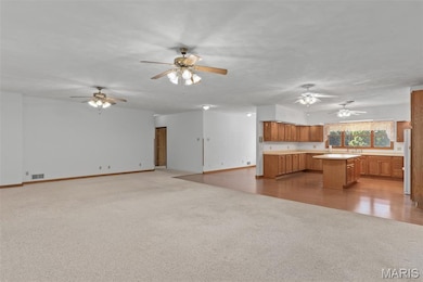 Kitchen featuring open floor plan, light countertops, light carpet, brown cabinetry, and a center island