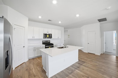 Kitchen featuring appliances with stainless steel finishes, an island with sink, white cabinetry, recessed lighting, and light wood finished floors