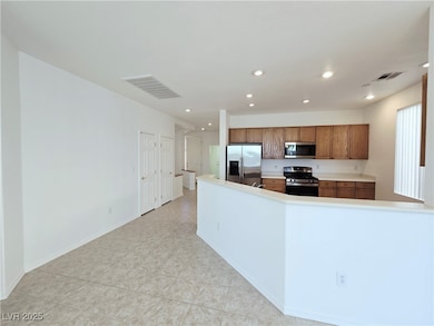 Kitchen featuring recessed lighting, stainless steel appliances, light countertops, brown cabinets, and a peninsula