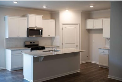 Kitchen with tasteful backsplash, white cabinetry, crown molding, light stone countertops, and stainless steel appliances