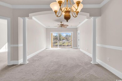 Carpeted spare room featuring ornate columns, ornamental molding, ceiling fan, and a chandelier