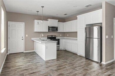 Kitchen with white cabinetry, appliances with stainless steel finishes, kitchen peninsula, decorative light fixtures, and sink