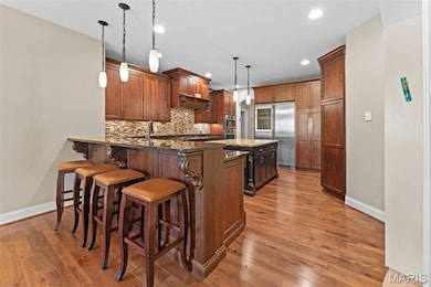 Kitchen featuring a kitchen breakfast bar, hanging light fixtures, built in fridge, backsplash, and light wood-style floors