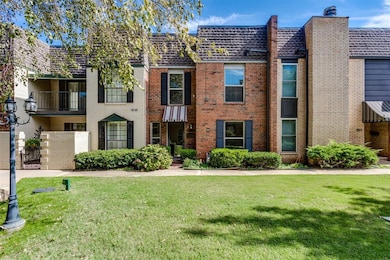View of front of property with brick siding, a front yard, a balcony, mansard roof, and a shingled roof