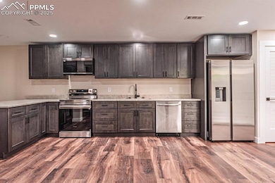 Kitchen featuring stainless steel appliances, recessed lighting, dark wood-style flooring, light stone counters, and dark brown cabinetry