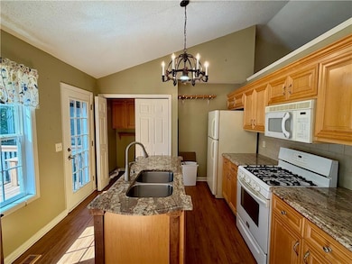 Kitchen with white appliances, vaulted ceiling, dark wood-style floors, light stone countertops, and hanging light fixtures