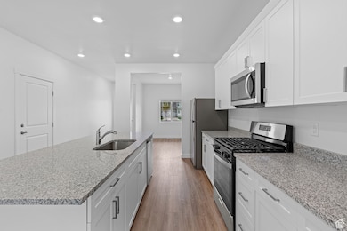 Kitchen with white cabinets, a sink, recessed lighting, wood finished floors, and stainless steel appliances