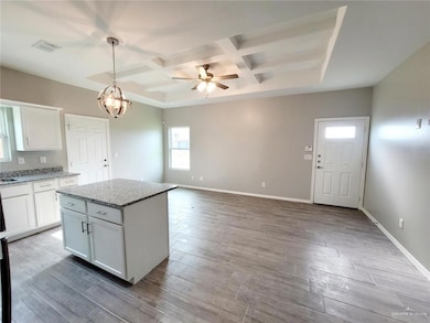 Kitchen featuring coffered ceiling, white cabinets, a ceiling fan, hanging light fixtures, and light stone countertops