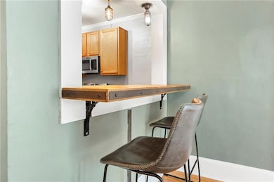Kitchen with stainless steel microwave, ornamental molding, a breakfast bar, light brown cabinets, and baseboards