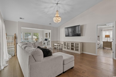Living room with a chandelier, wood finished floors, and vaulted ceiling