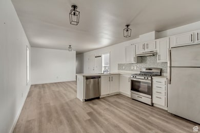 Kitchen featuring appliances with stainless steel finishes, light countertops, white cabinets, and backsplash