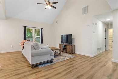 Living room featuring high vaulted ceiling, attic access, light wood-style floors, and a ceiling fan