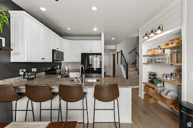 Kitchen with black microwave, stainless steel electric range oven, a sink, a peninsula, and light wood-style floors