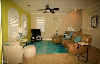 Living room featuring a ceiling fan, crown molding, stairs, carpet flooring, and tile patterned flooring