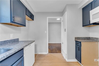 Kitchen with white appliances, blue cabinets, and light hardwood flooring