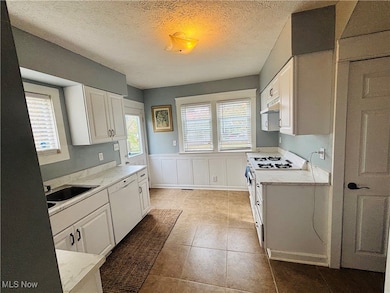 Kitchen with white cabinetry, a textured ceiling, wainscoting, white appliances, and light tile patterned flooring