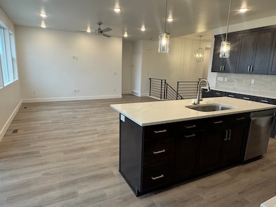 Kitchen featuring dark cabinetry, decorative backsplash, an island with sink, open floor plan, and dishwasher