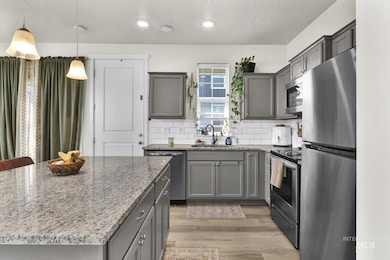 Kitchen with stainless steel appliances, light stone countertops, gray cabinets, light wood-type flooring, and backsplash