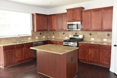 Kitchen featuring stainless steel appliances, dark wood-style flooring, light stone counters, and a kitchen island