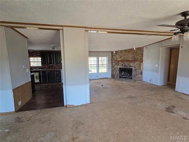 Unfurnished living room with a wainscoted wall, a ceiling fan, a fireplace, a textured ceiling, and a decorative wall
