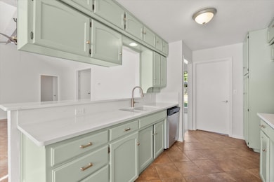 Kitchen featuring green cabinetry, light tile patterned floors, and stainless steel dishwasher