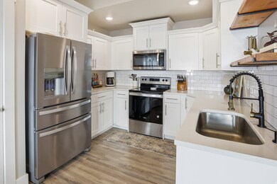 Kitchen with stainless steel appliances, white cabinets, backsplash, light stone counters, and recessed lighting