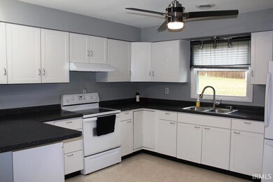 Kitchen featuring white appliances, white cabinets, dark countertops, and under cabinet range hood