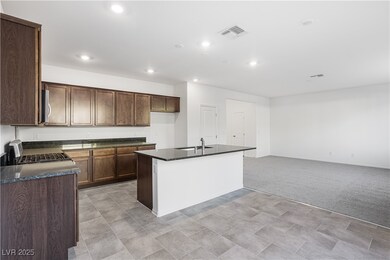 Kitchen with a kitchen island with sink, appliances with stainless steel finishes, light colored carpet, recessed lighting, and dark brown cabinetry