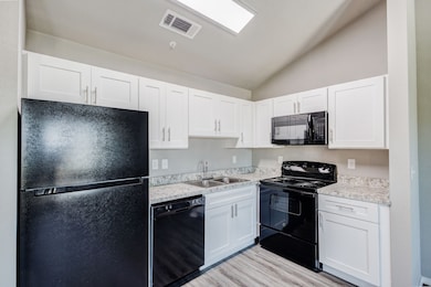 Kitchen with black appliances, lofted ceiling, white cabinetry, light wood-style flooring, and light stone counters